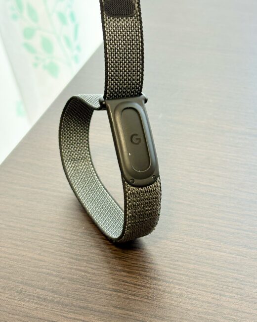 机の上で立てたGoogle Fitbit Air。本体裏面のGoogleロゴのアップ