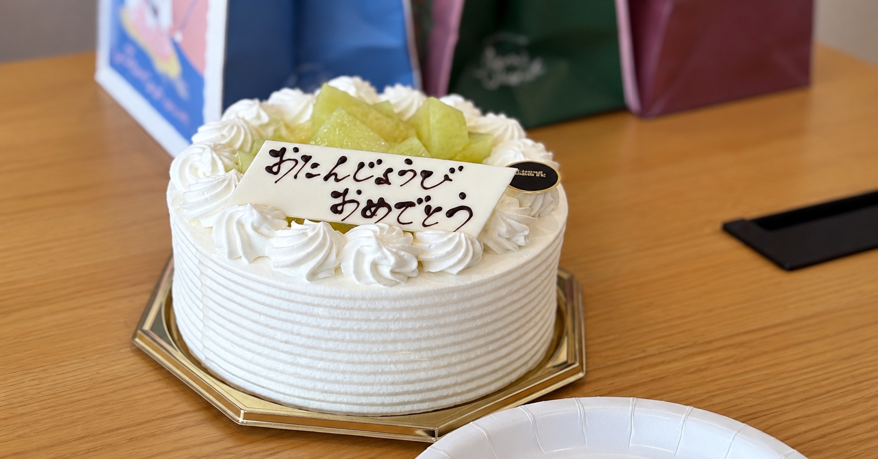 「おたんじょうびおめでとう」のプレートが乗った白いホールケーキが、テーブルの上に置かれている写真