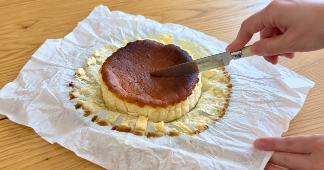 焼き色のついたチーズケーキにナイフを入れている手元の写真