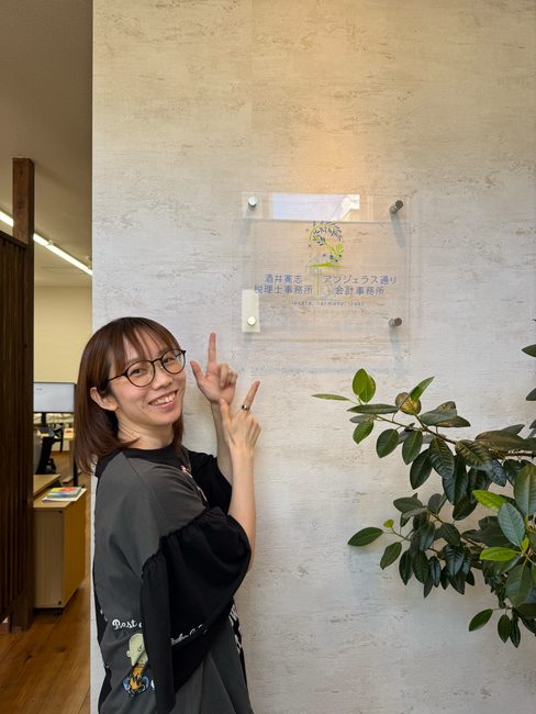 事務所の看板の前で笑顔を見せる講師のChanさん