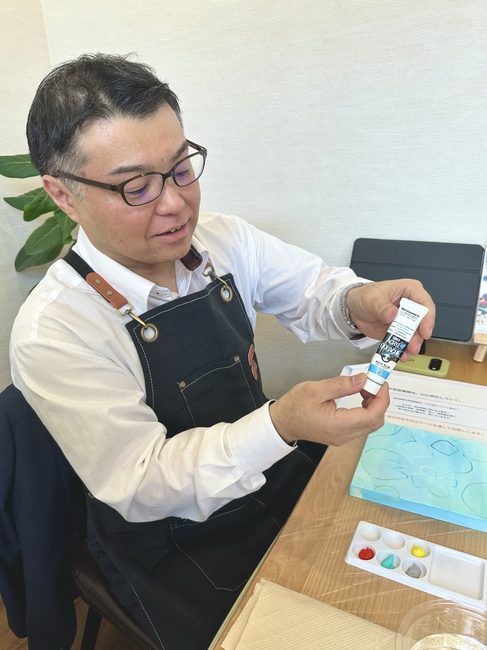 エプロン姿で絵の具のチューブを手に取り、自分の色を選ぶ酒井